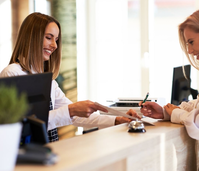 Image of receptionist talking to a customer while the customer is writing something on the document